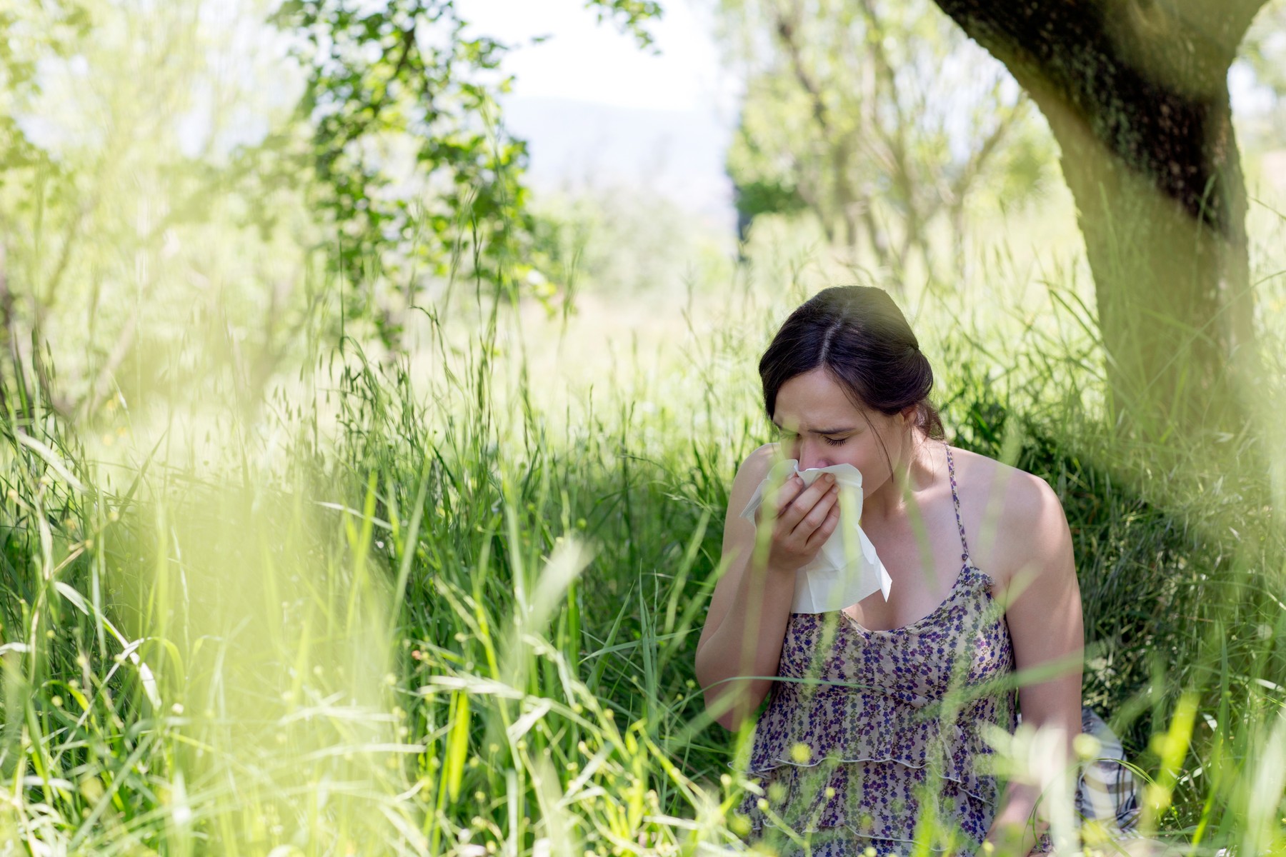 Young woman in tall grass sneezing into handkerchief alergija