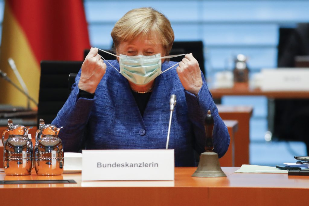 German Chancellor Angela Merkel takes down her face mask as she arrives for the weekly cabinet meeting of the German government at the chancellery in Berlin, Germany, Wednesday, Oct. 7, 2020. (AP Photo/Markus Schreiber, Pool)