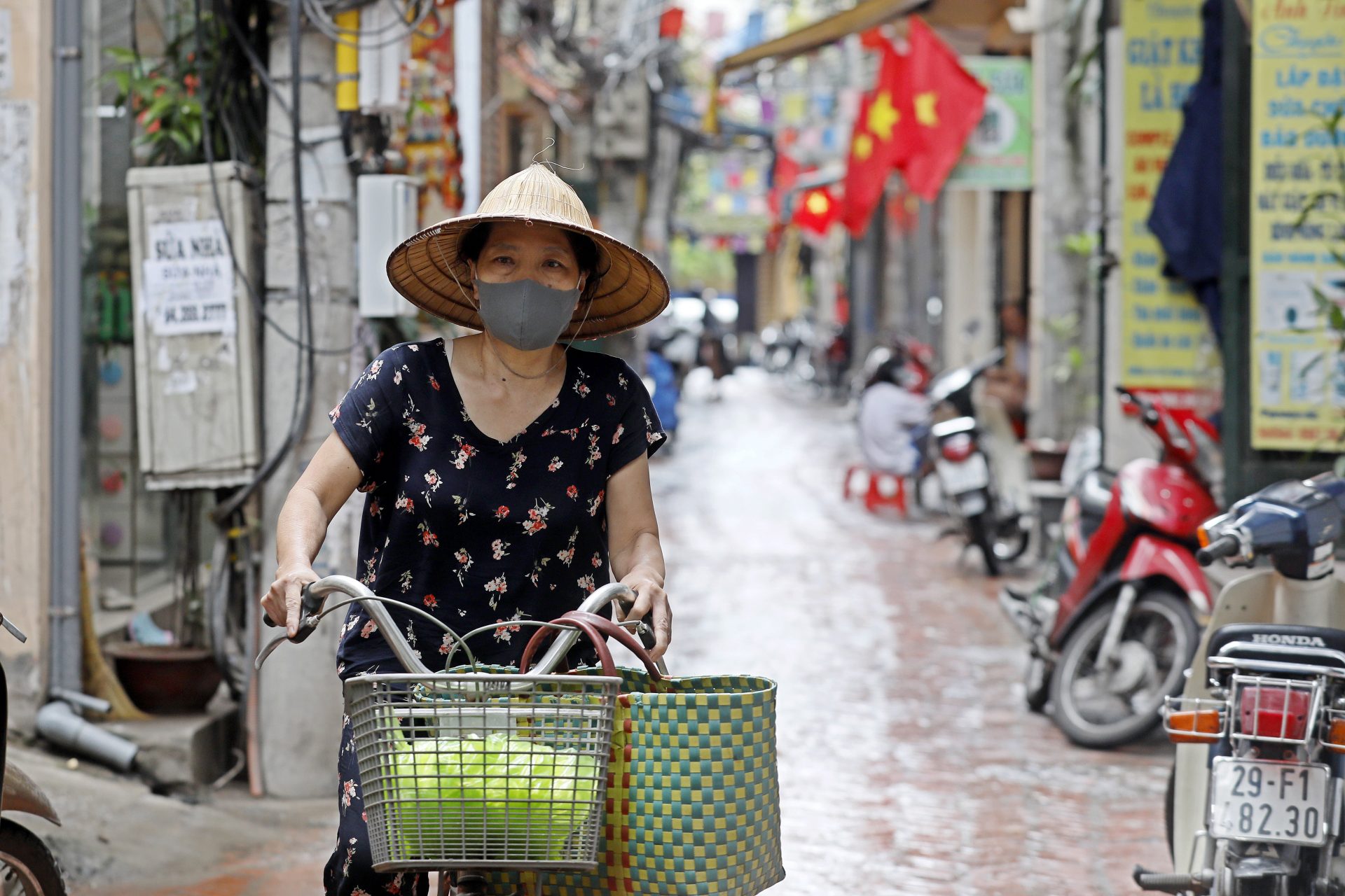 epa08587164 A woman wearing a face mask rides a bicycle in an alley of Hanoi, Vietnam, 06 August 2020. Vietnam has recently seen an uptick in coronavirus cases after being free of domestically transmitted infections for 100 days.  EPA-EFE/LUONG THAI LINH