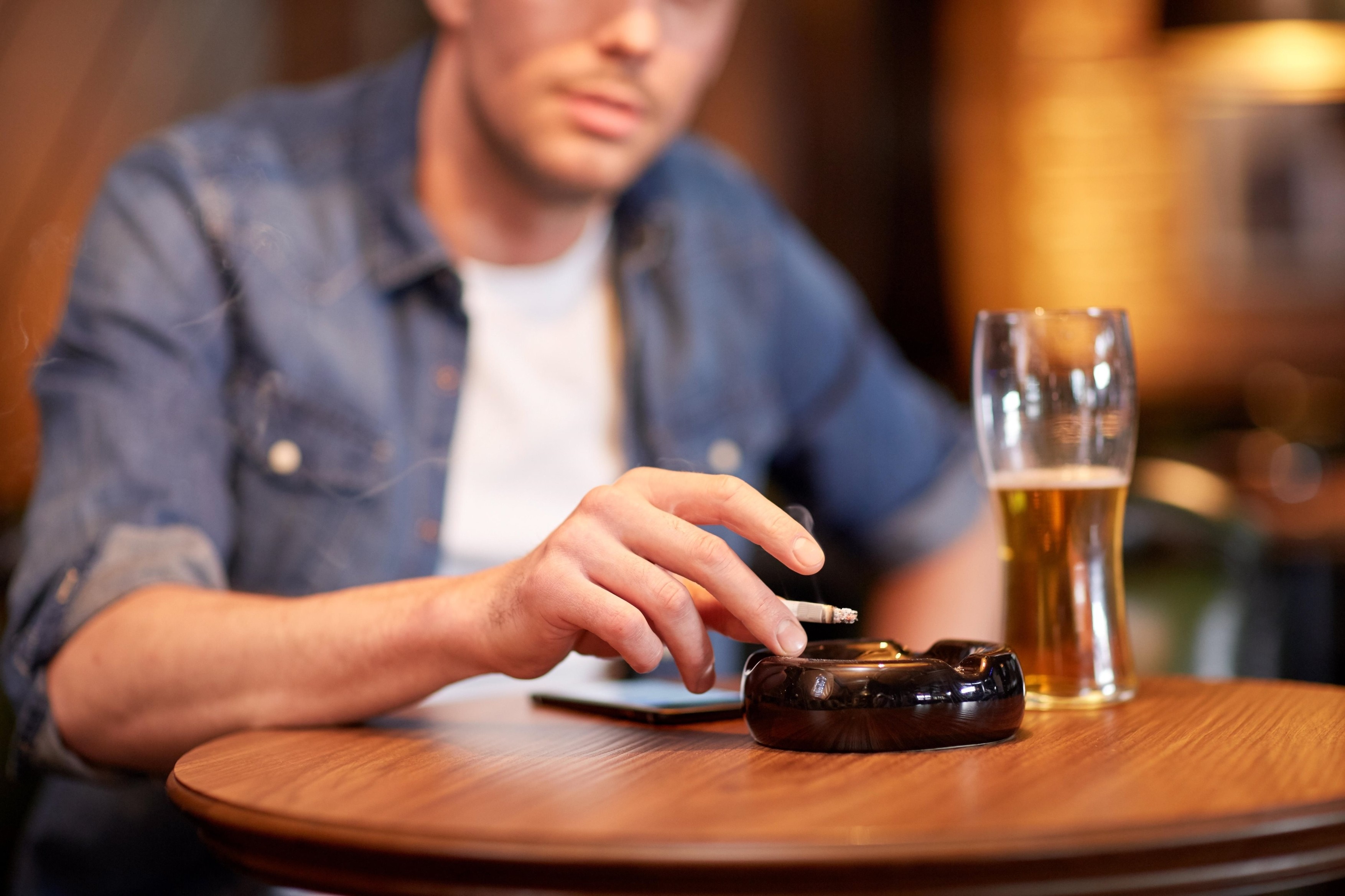 man drinking beer and smoking cigarette at bar