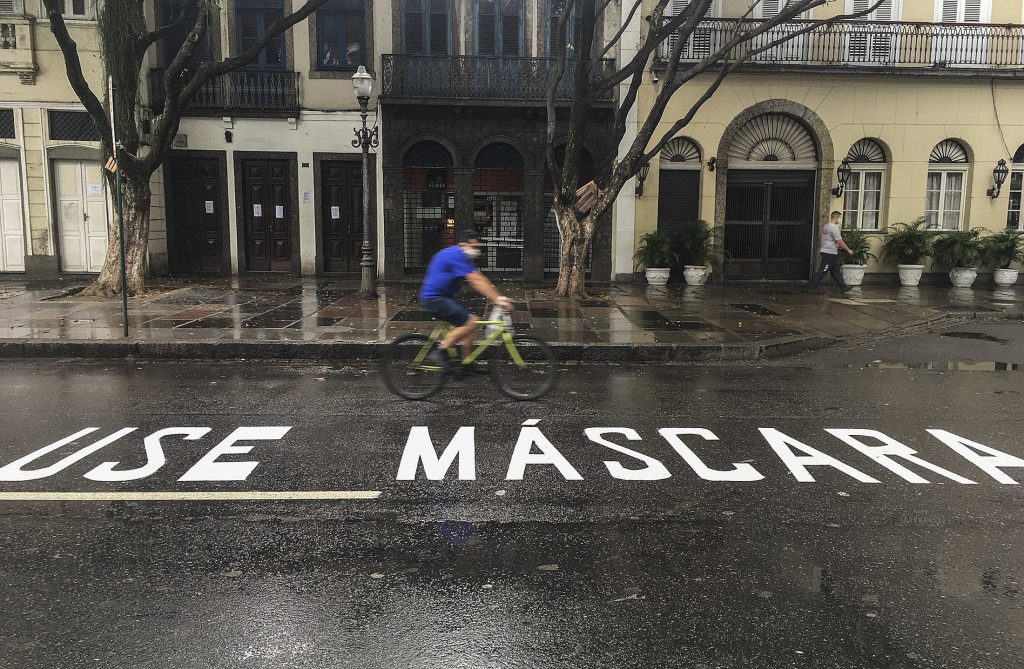 epa08399067 A man wears a mask as he rides a bicycle over a street with a sign that reads 'Wear  a mask' in Rio de Janeiro, Brazil, 03 May 2020.  EPA-EFE/Antonio Lacerda