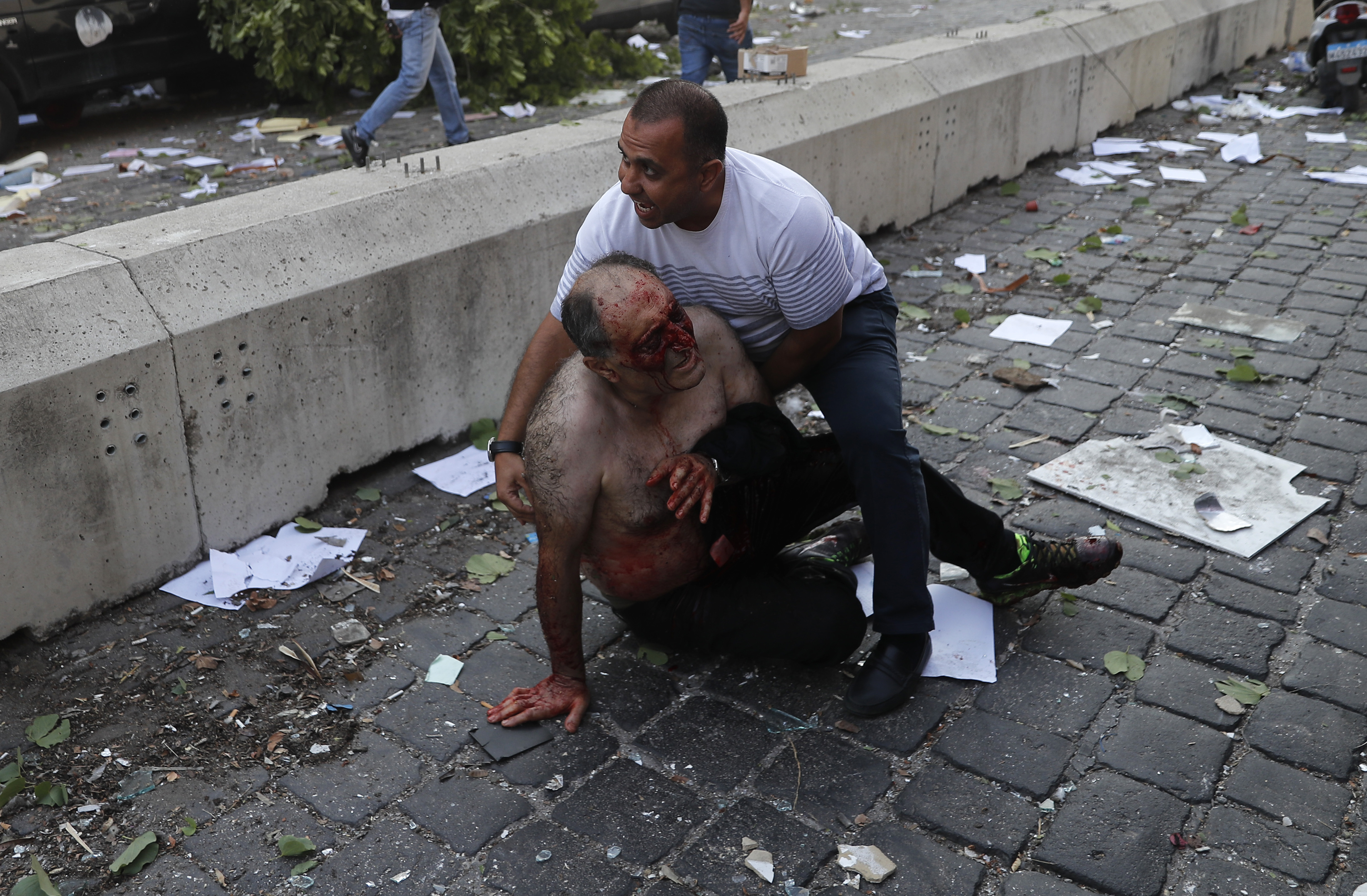 A Lebanese man helps an injured person who was wounded by an explosion that hit the seaport, in Beirut Lebanon, Tuesday, Aug. 4, 2020. (AP Photo/Hussein Malla)