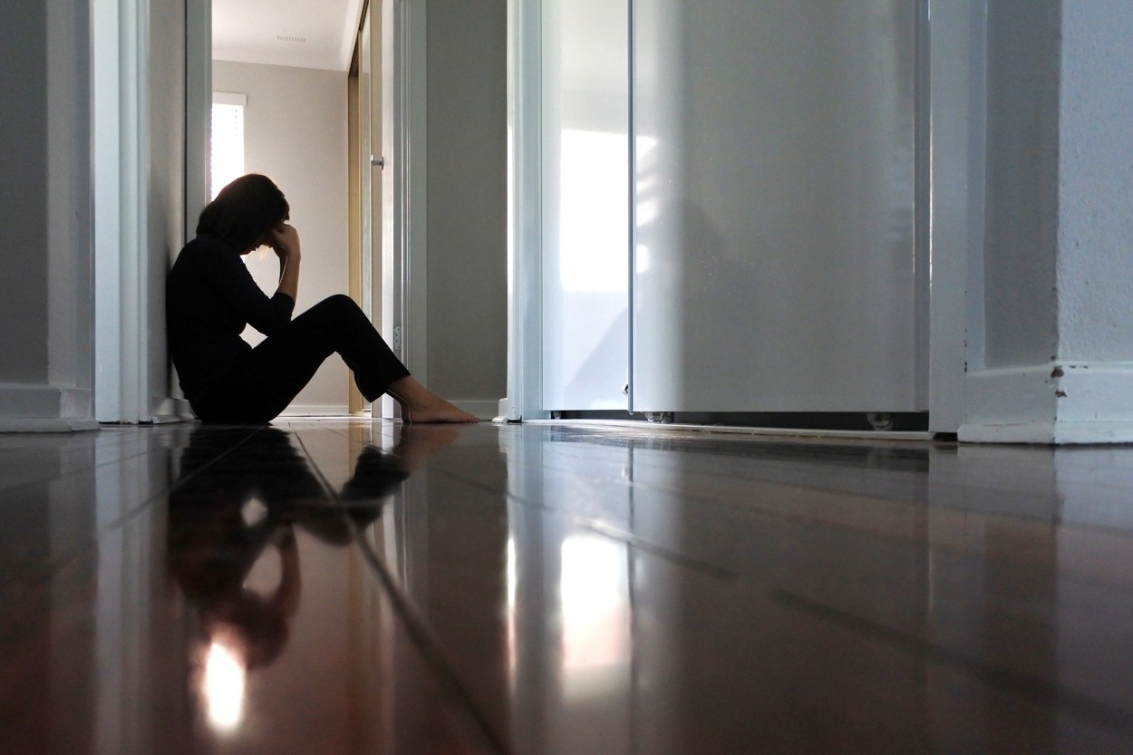 Sad woman sitting on dark home corridor floor