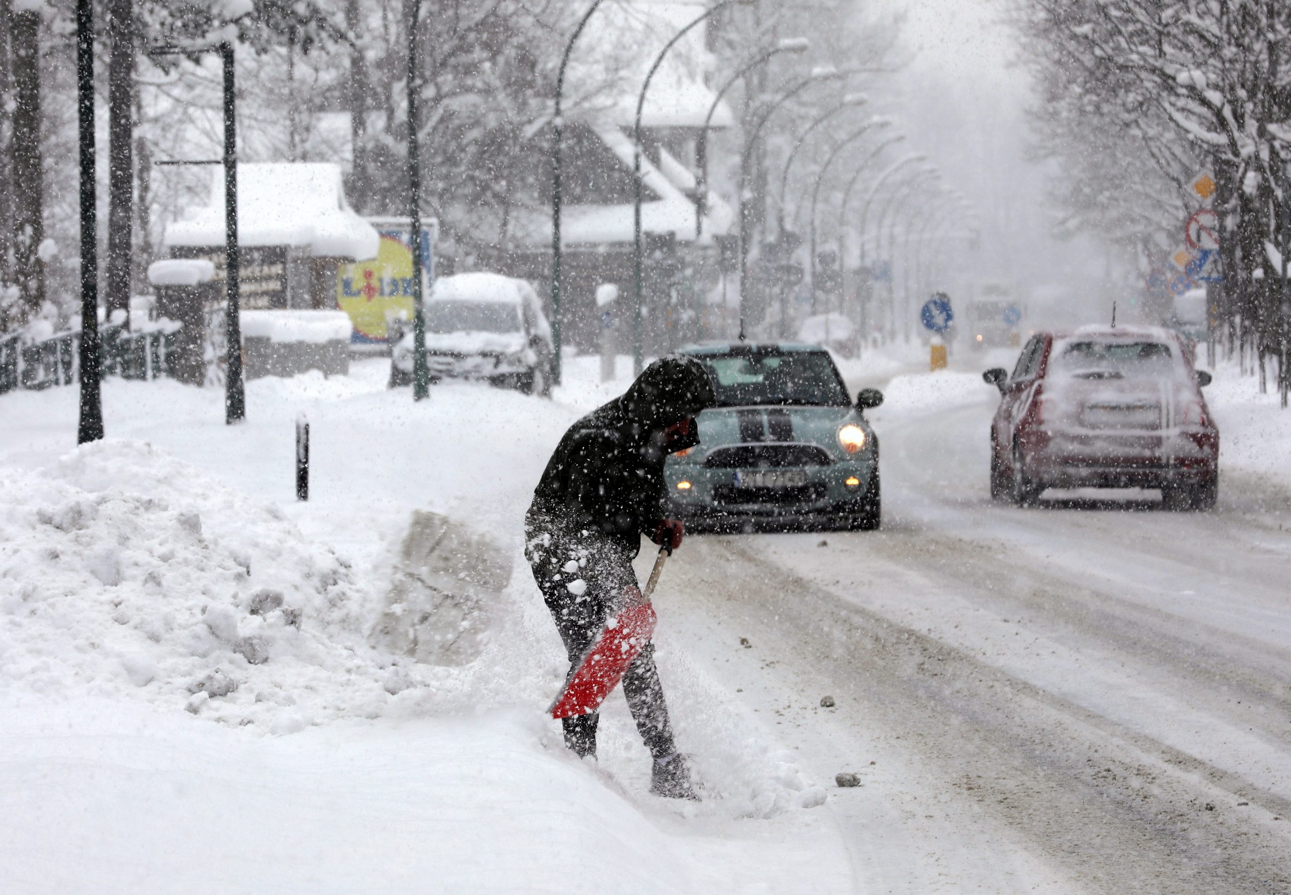 Poljska, 23.03.2020. Sneg
epa08314758 A person shovels snow as cars drive by on a snow-covered road on a wintery morning in Zakopane, south Poland, 23 March 2020.  EPA-EFE/Grzegorz Momot POLAND OUT