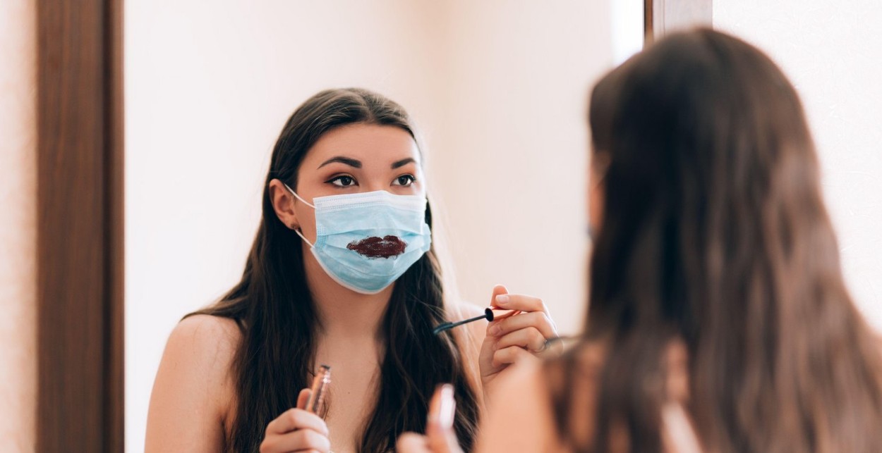 Young beautiful girl makes a make-up in medical mask