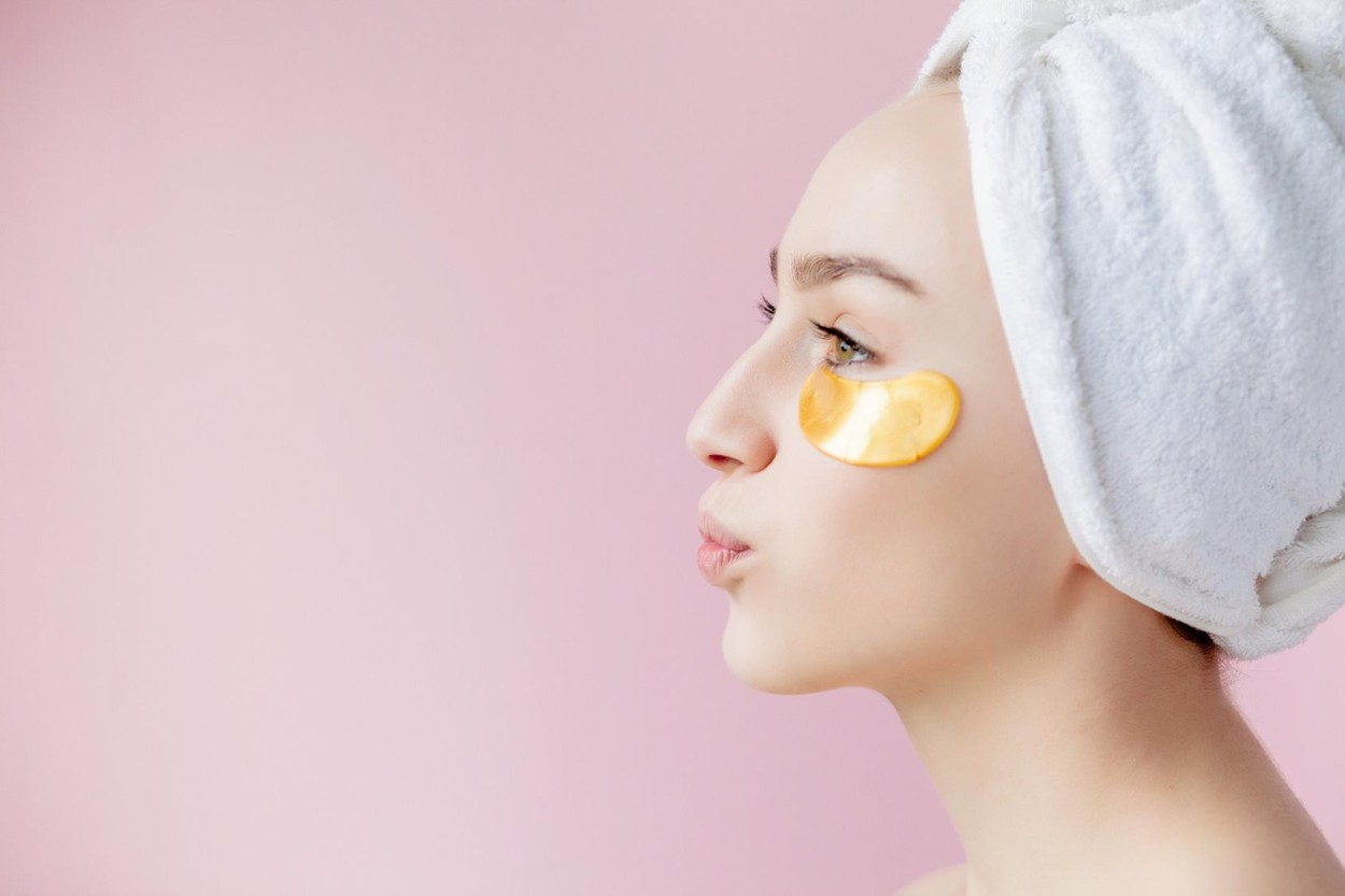 Portrait of Beauty Woman with Eye Patches on pink background. Woman Beauty Face with Mask under Eyes. Beautiful Female with natural Makeup and Gold Co