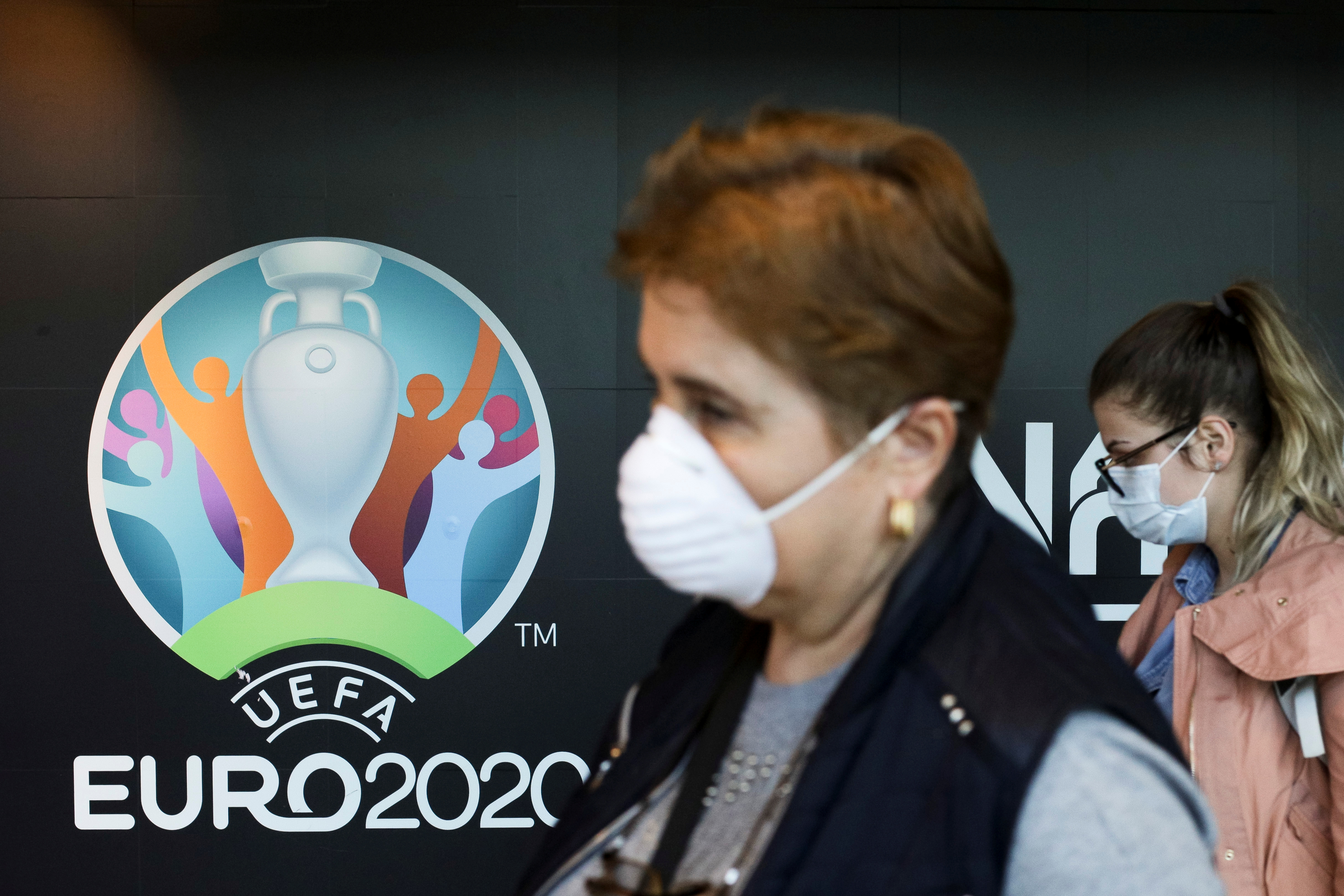 Travellers pass by a logo of the 2020 UEFA European Football Championship displayed on a wall inside Bucharest Henri Coanda International Airport