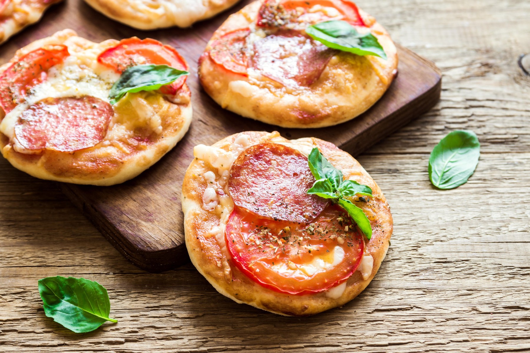 Mini Pizzas - Fresh homemade mini pizzas with pepperoni, cheese, tomatoes and basil on rustic wooden background.