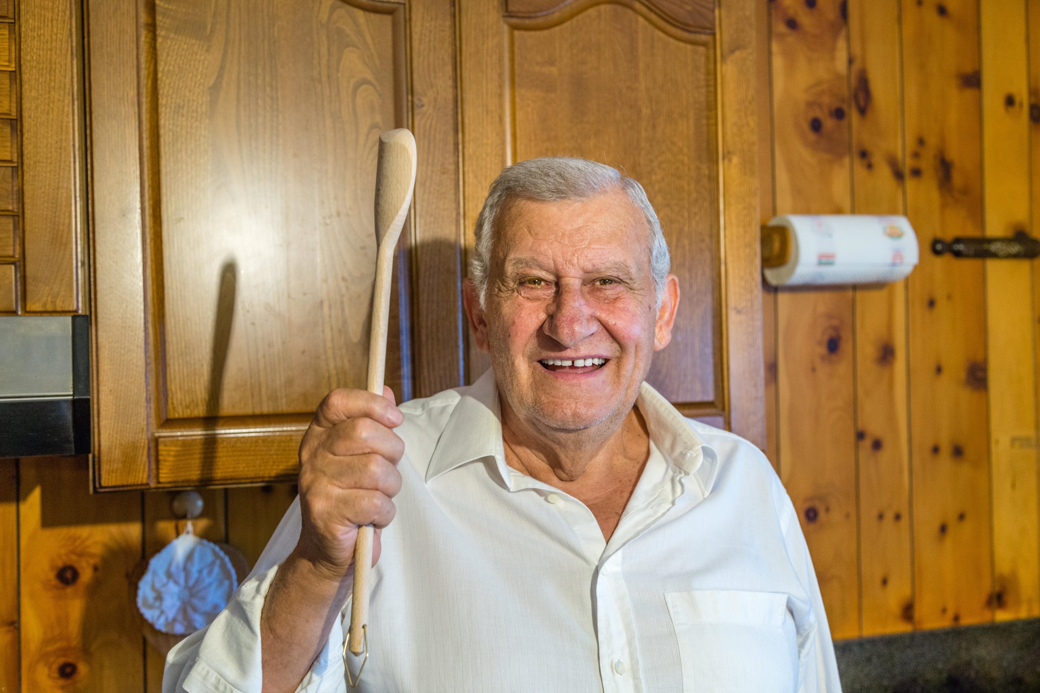 elderly man holding wooden cooking spoon while smiling in vintage kitchen