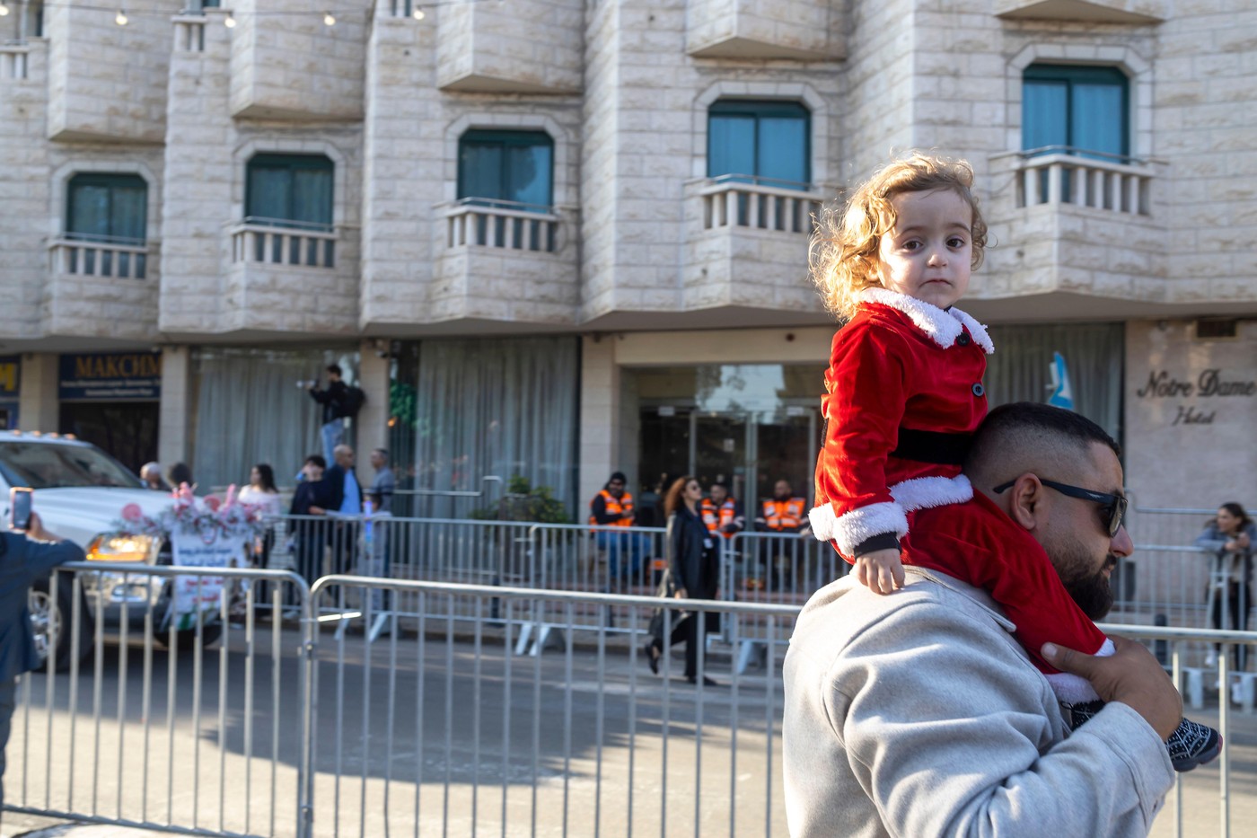 Nazareth, Israel, December 24, 2025  Young child dressed in a Santa costume sitting on their father's shoulders watching the Christmas parade in Nazar