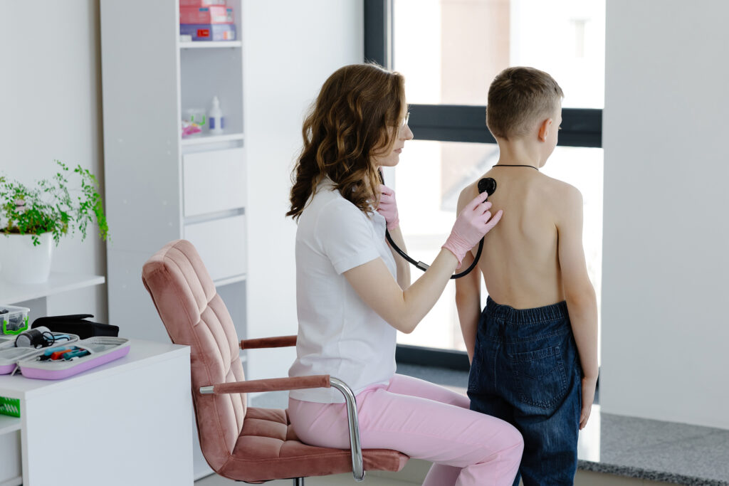 Boy stands in front woman doctor with stethoscope in hand undergoes routine medical examination by professional pediatrician in office of children clinic. deca bolest, virusi bakterije