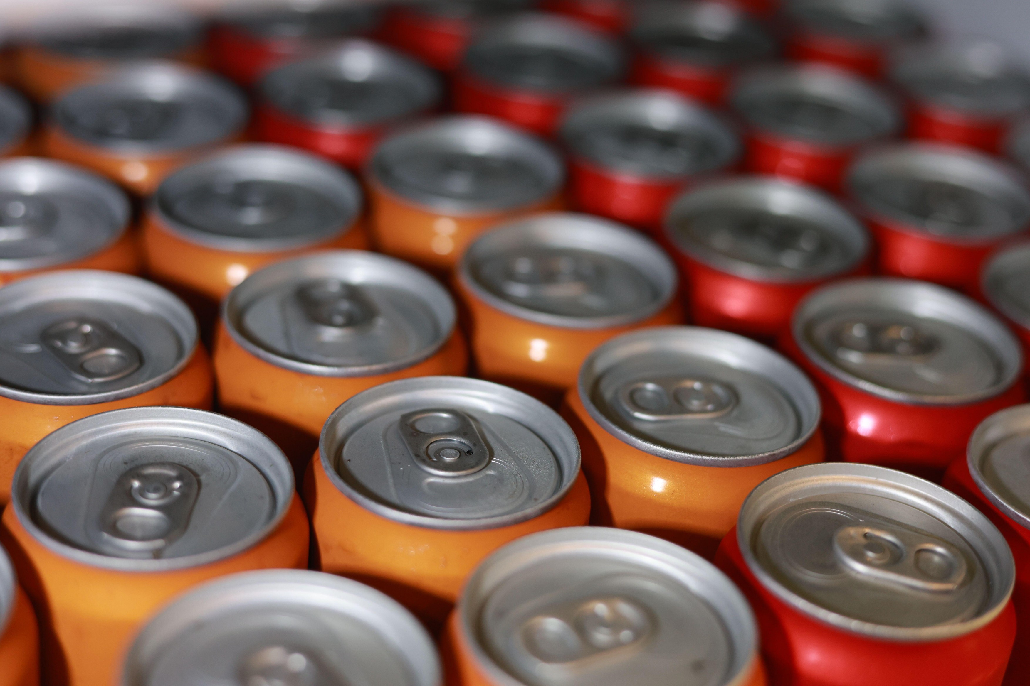 Top view of many red and orange aluminum beverage cans in pattern. close up background of cold soda ready for refreshment, representing thirst and con