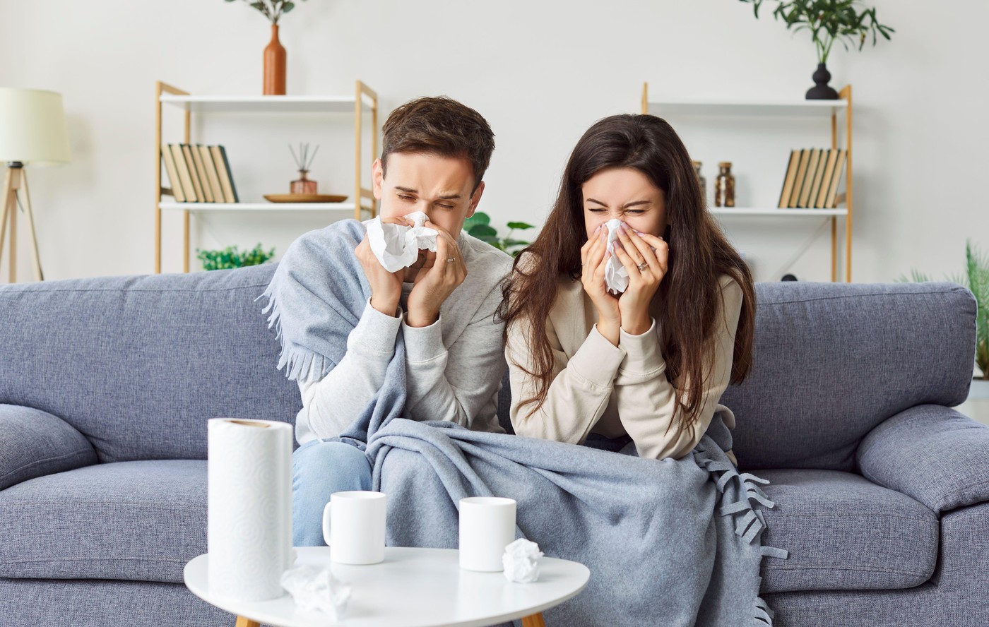 Sick Husband and Wife Sneezing Together on Couch at Home