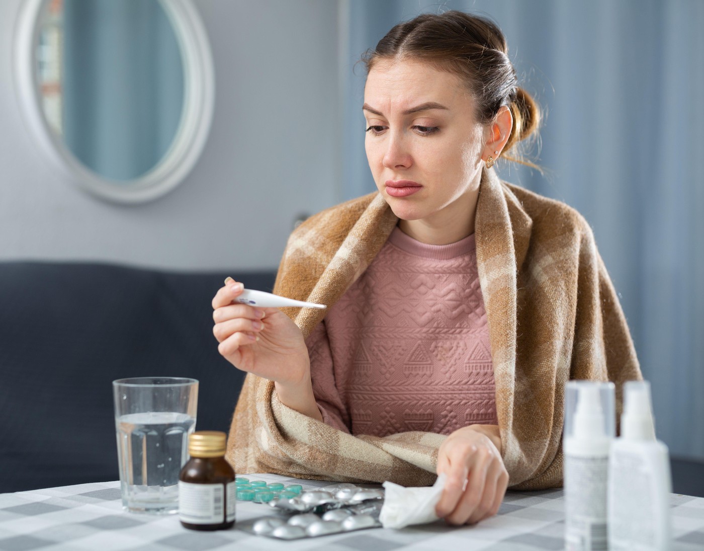 Woman with flu sitting at table with medicines and holding thermometer.,Image: 1010537692, License: Royalty-free, Restrictions: , Model Release: no, Credit line: Iakov Filimonov / Alamy / Profimedia