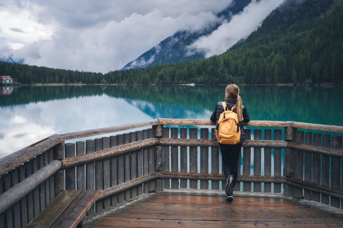 Woman with yellow backpack standing on wooden terrace near lake