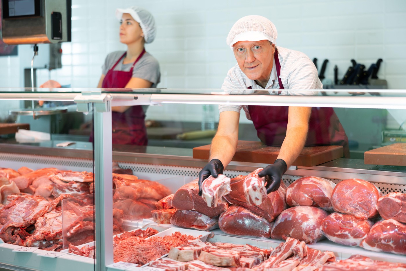 Elderly butcher shop salesman offering fresh raw beef short ribs