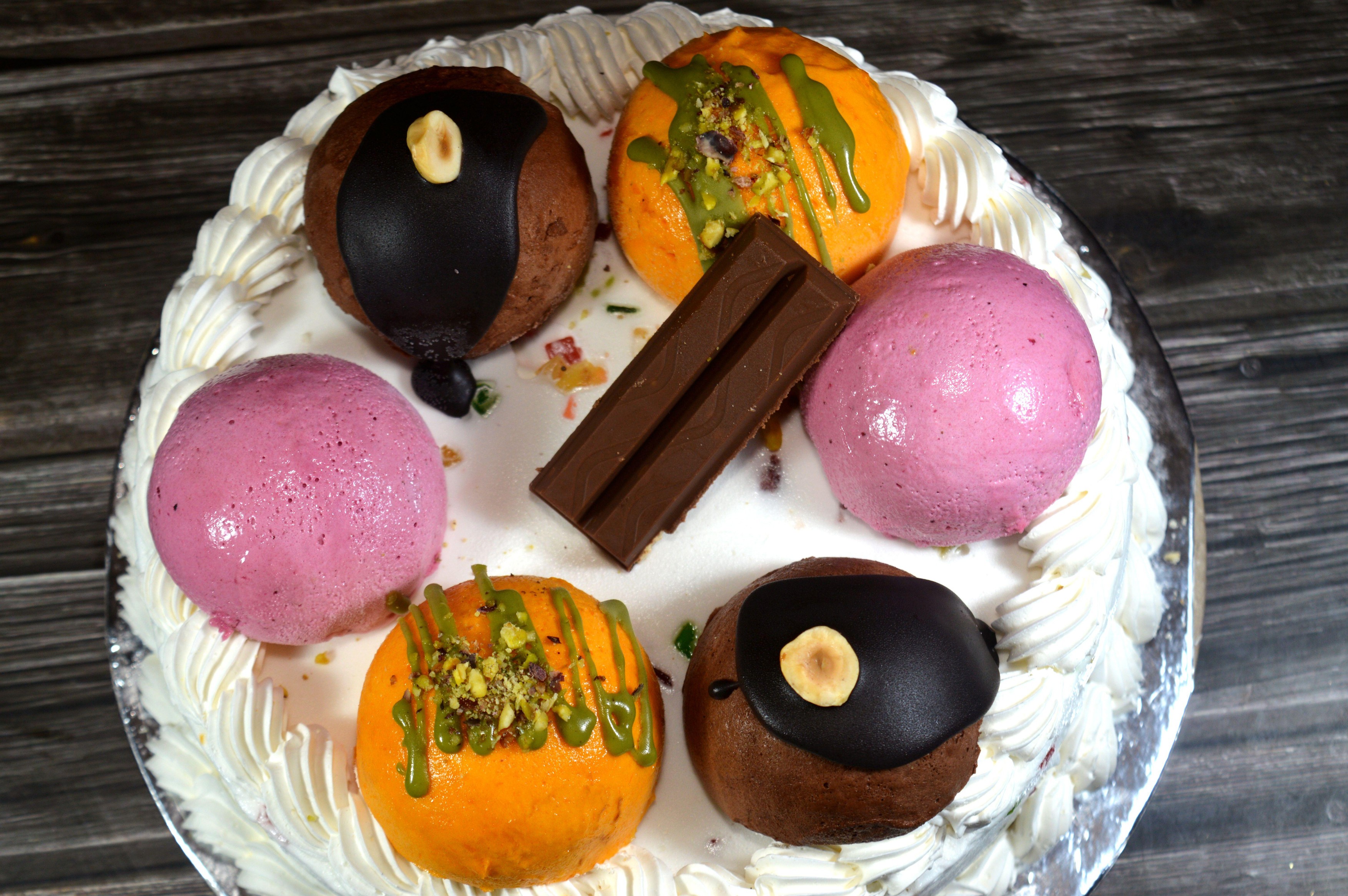 Cassata ice cream cake, vanilla, whipped cream, milk, filled with dried fruit, topped with mango balls with pistachio pieces and sauce, chocolate bars