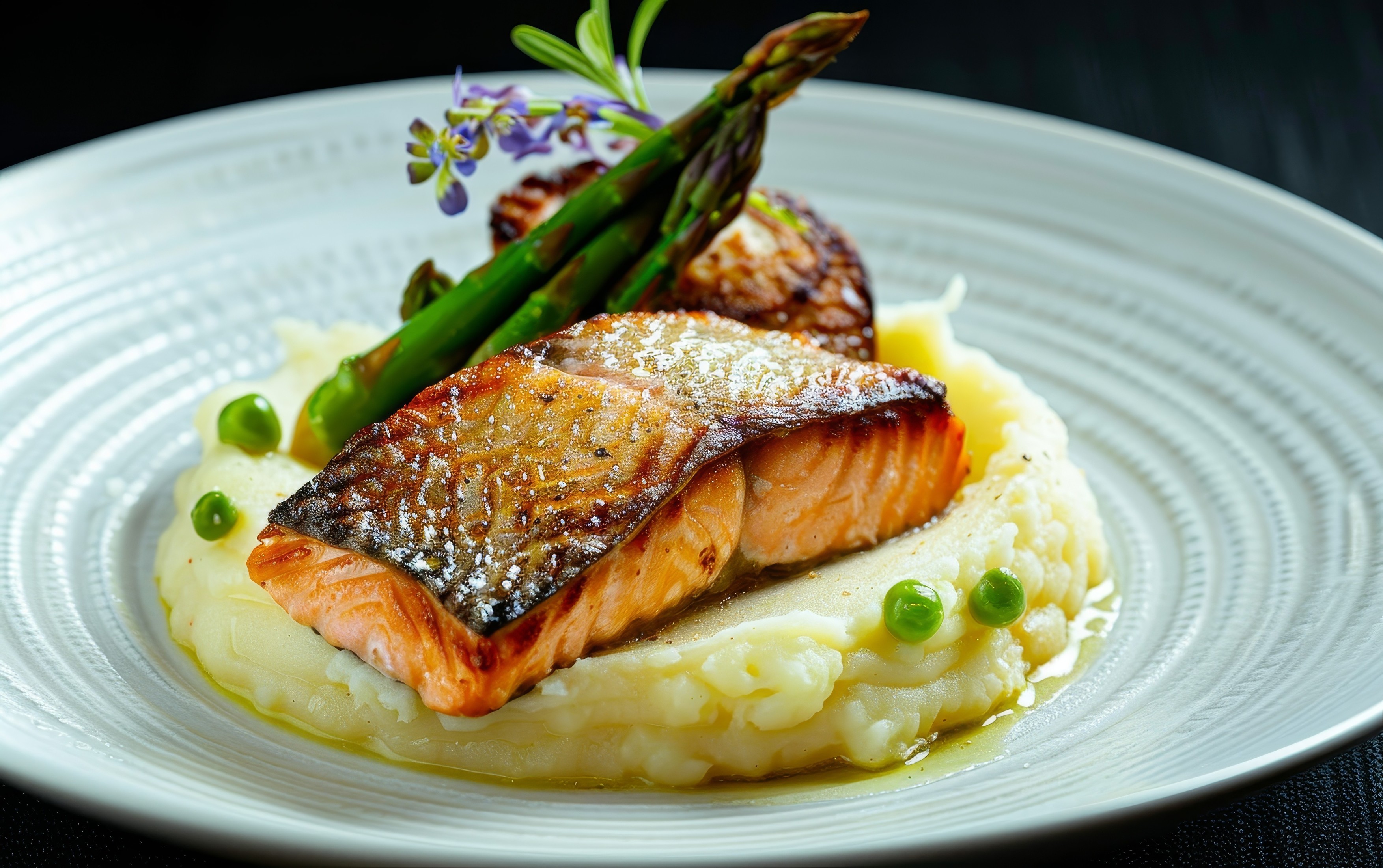 A beautifully seared salmon fillet rests on a velvety mound of mashed potatoes, accented by asparagus spears and a delicate sauce.