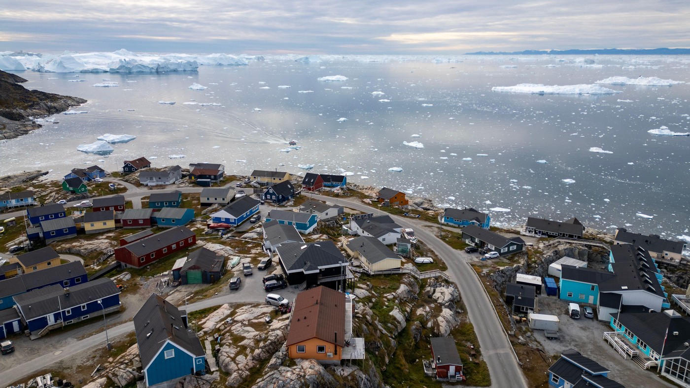 This aerial photograph showcases the colorful houses of Ilulissat, a coastal town in Greenland. The town is situated on rocky terrain overlooking an i