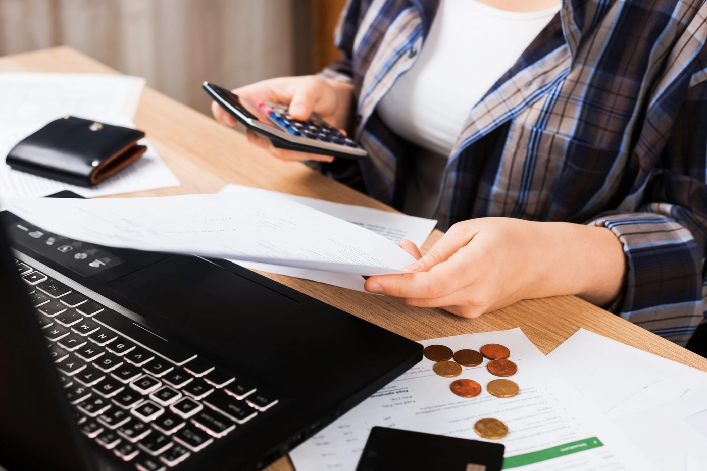 Woman checking bills and using a calculator near a laptop. Household budget concept with coins, credit card and documents on the table. High quality p