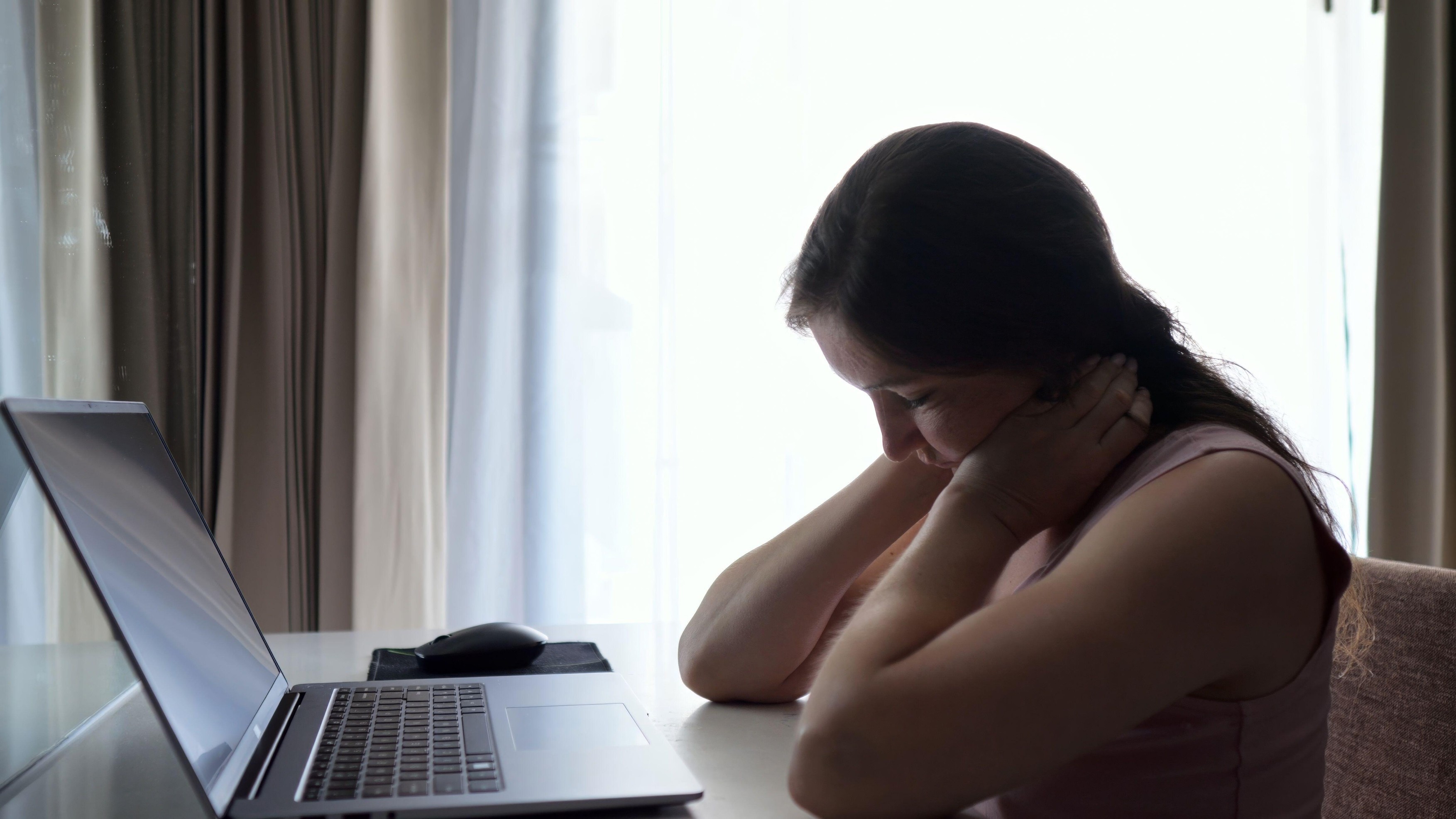 Woman types on laptop in quiet hotel room pausing to stretch neck