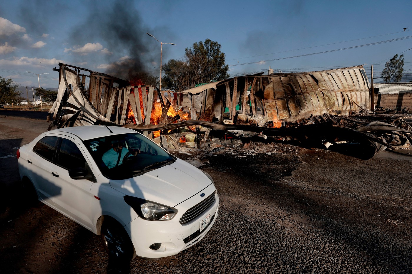A car passes by a burned truck, allegedly set on fire by organised crime groups in response to an operation to arrest a high-priority security target, on a highway near Acatlan de Juarez, Jalisco state, Mexico on February 22, 2026