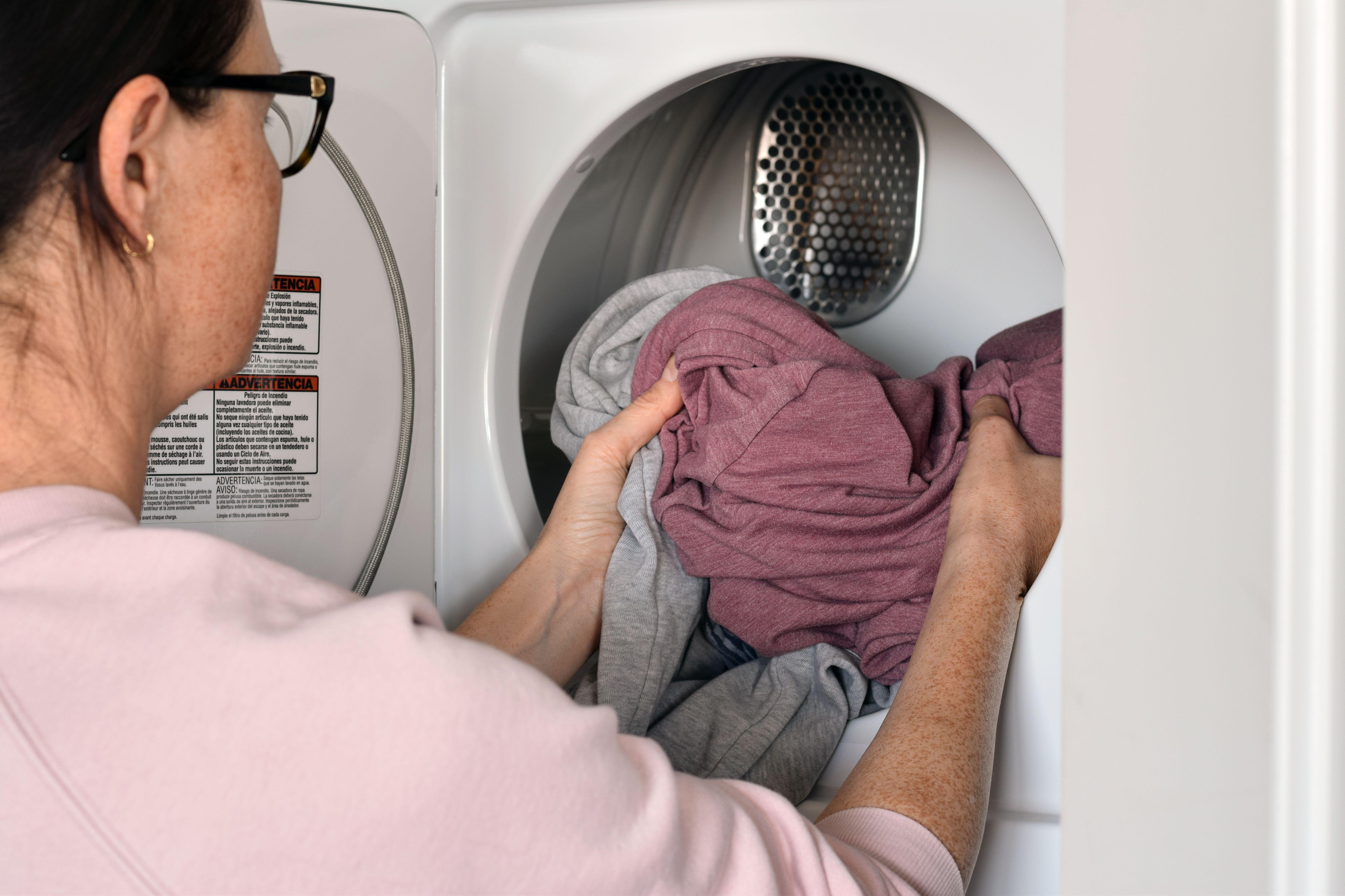 Woman taking freshly dried clothes out of a household clothes dryer