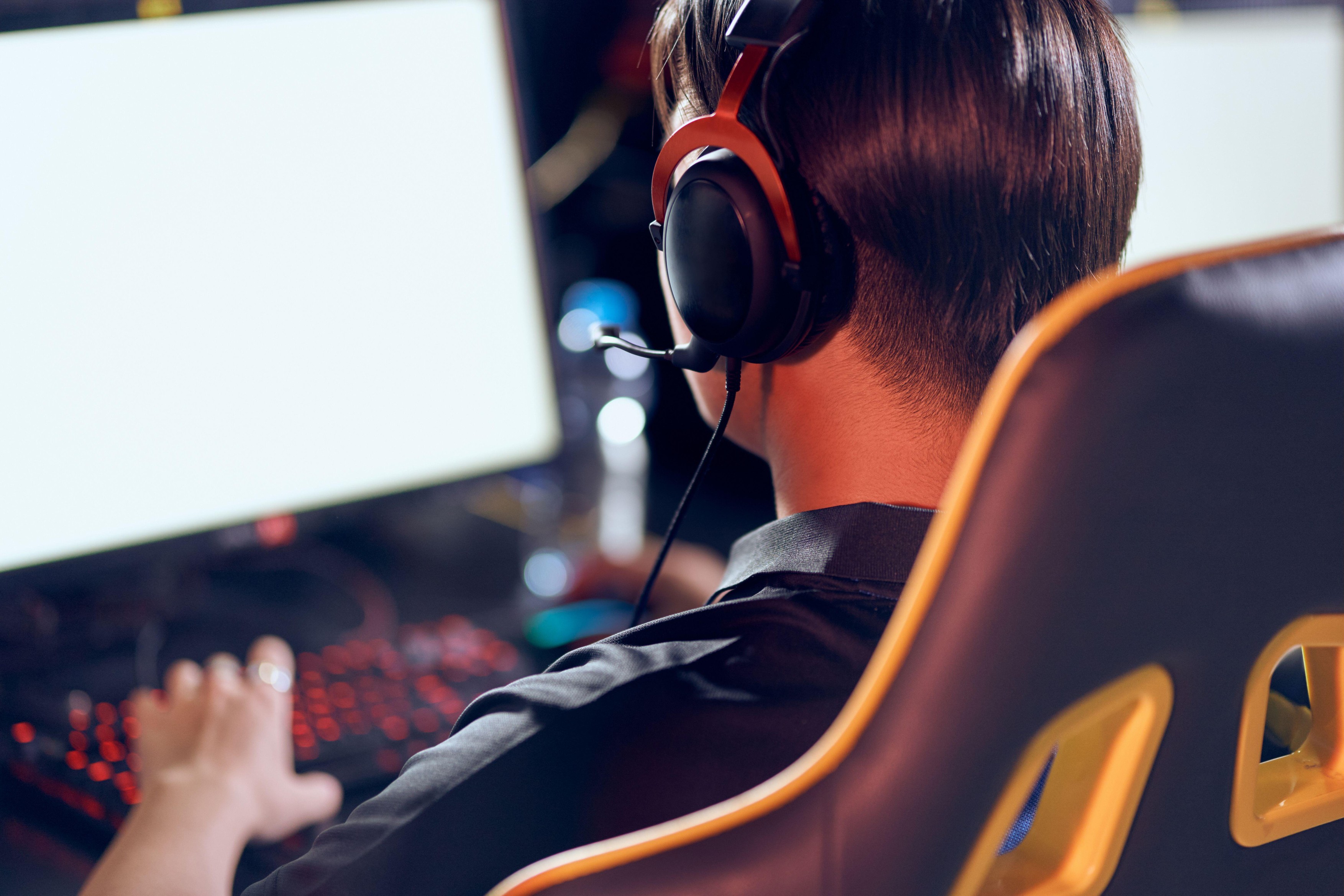 Rear view of a male cybersport gamer wearing headphones playing online video games while sitting in gaming club or in internet cafe.