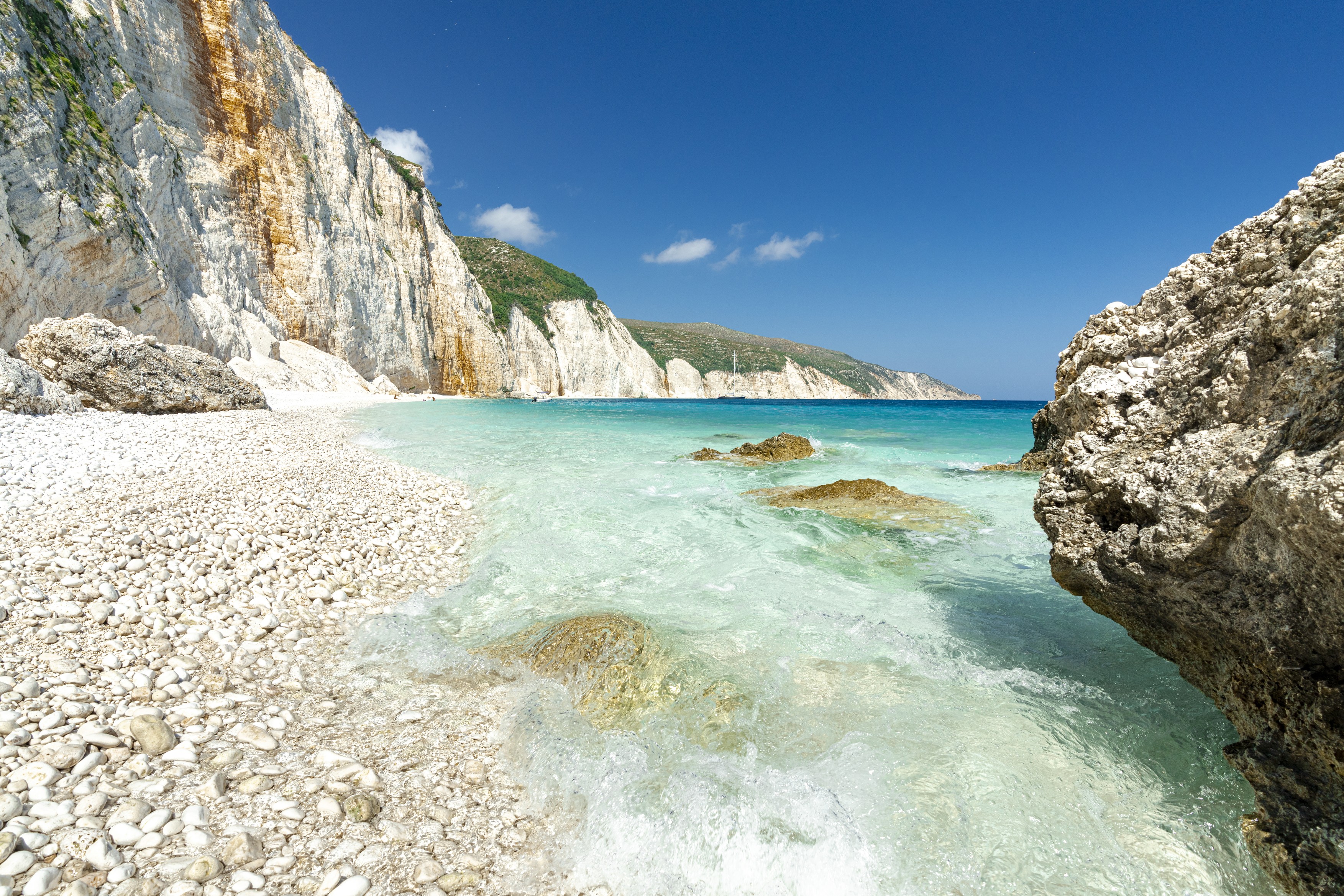 Waves of the turquoise clear sea washing the white stones of Fteri Beach