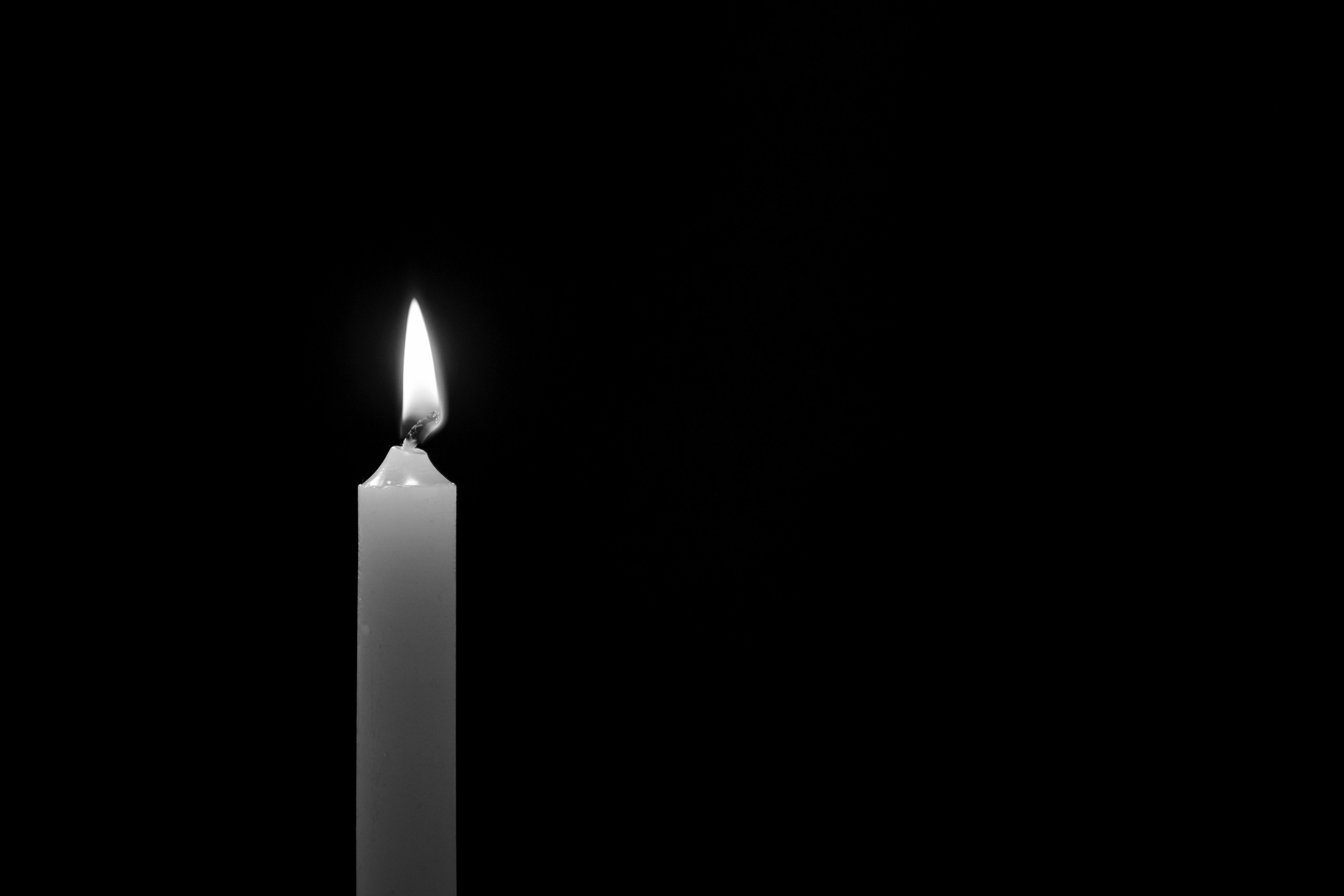 White candle on a black background, close up shot. Memory, symbol, religion, and prayer concepts.