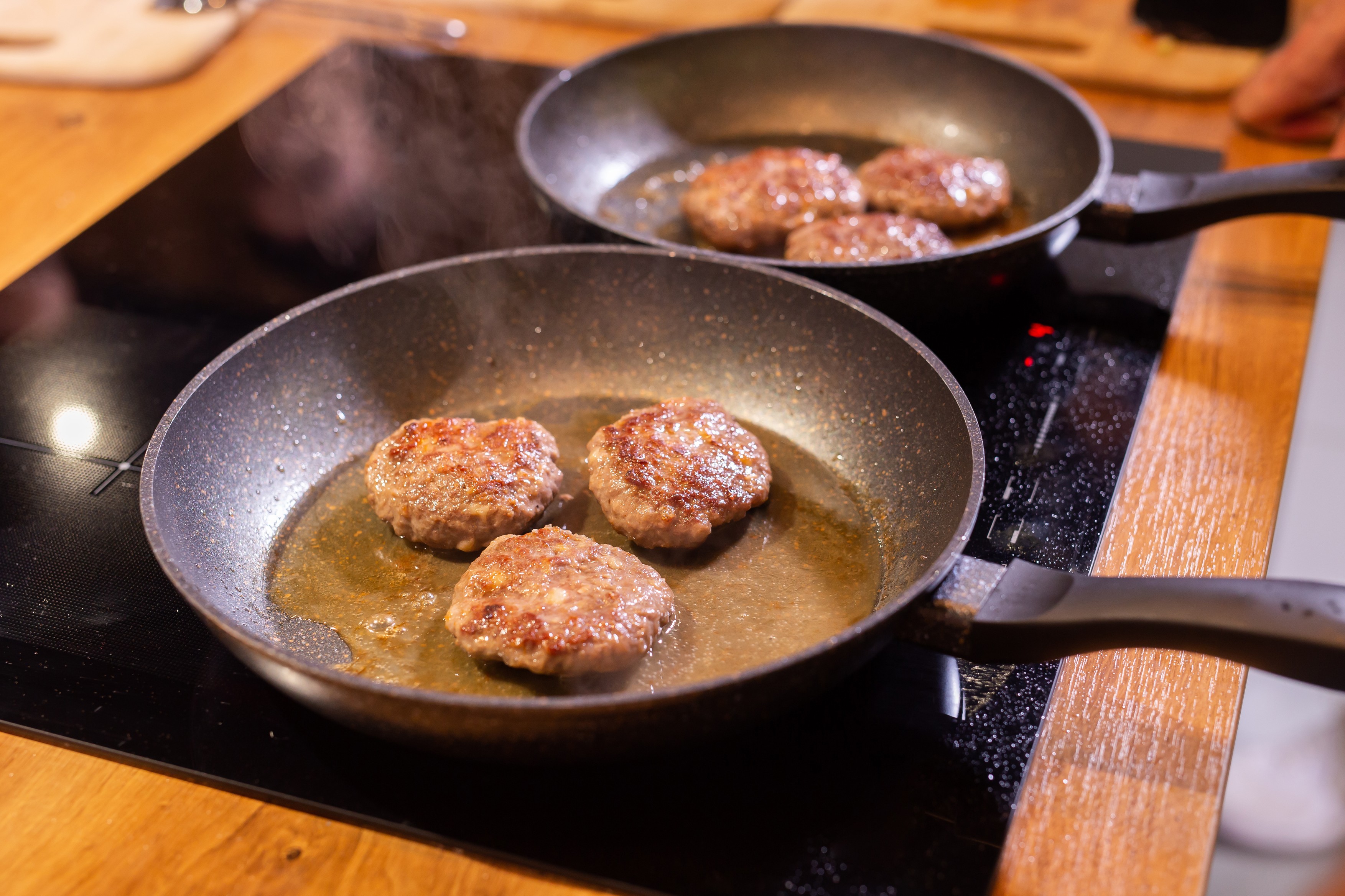 Meat burgers or cutlet-shaped patty being shallow fried in oil on a frying pan