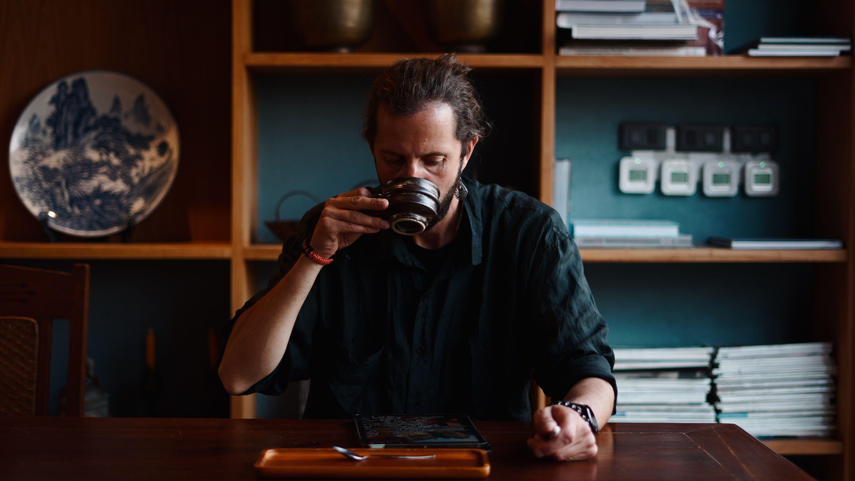 Man drinking hot tea from a cup, relaxing and observing a tablet